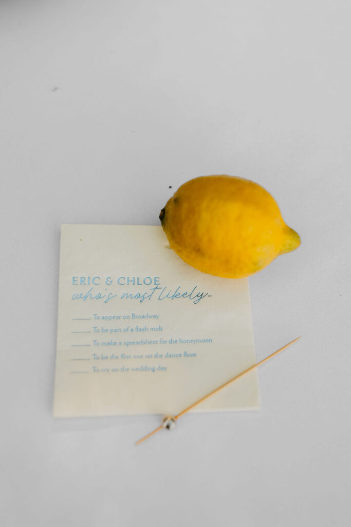 A lemon, a toothpick, and a card with "Eric & Chloe what’s most likely" and a checklist with various options are on a white surface.