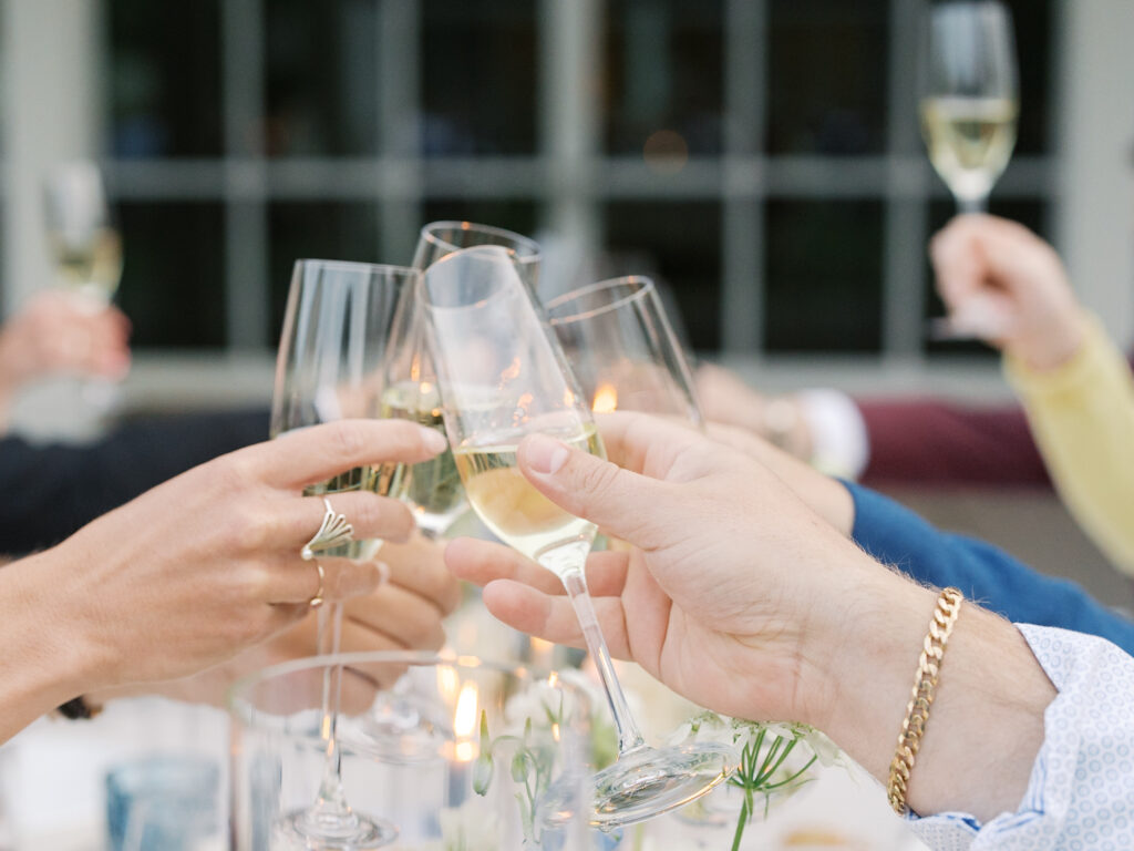A group of people clink champagne glasses together in a toast at a table set with candles and flowers, celebrating a beautiful Solage Calistoga wedding.