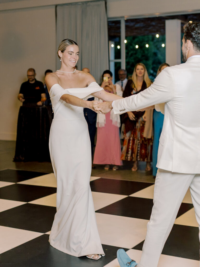 A bride and groom dance together on a black-and-white checkered floor at their Solage Calistoga wedding, with guests watching in the background.