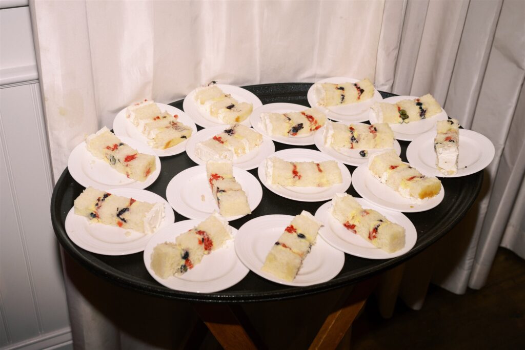 A round tray holds several small white plates, each with a slice of layered white cake filled with berries and cream. The tray is set against a white curtain background.