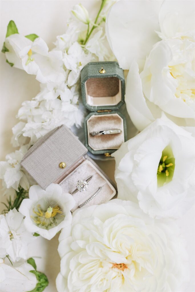 Two vintage-style rings in velvet boxes are displayed among white flowers, including roses and lisianthus.