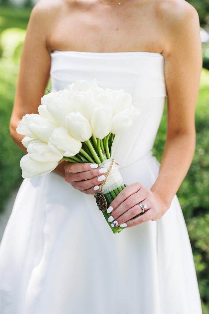 A person in a white strapless dress holds a bouquet of white tulips, displaying a ring and white manicured nails.
