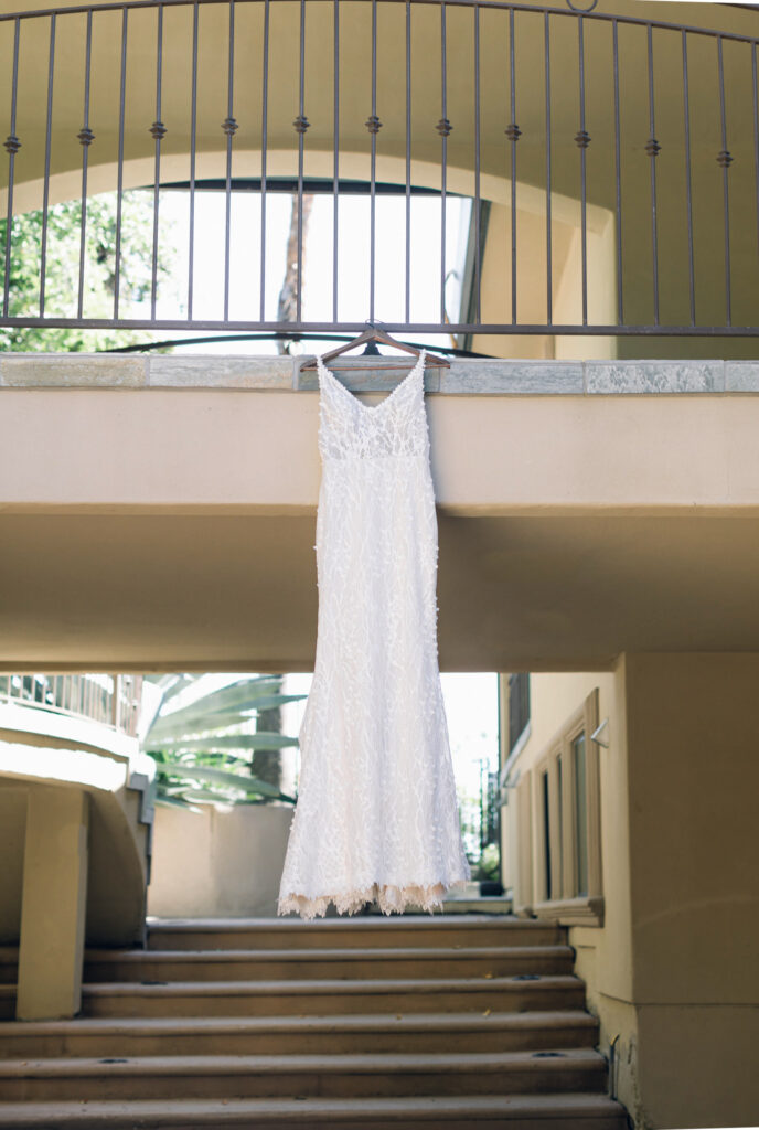 A white sleeveless lace dress is hanging from a railing above a staircase outside a building.
