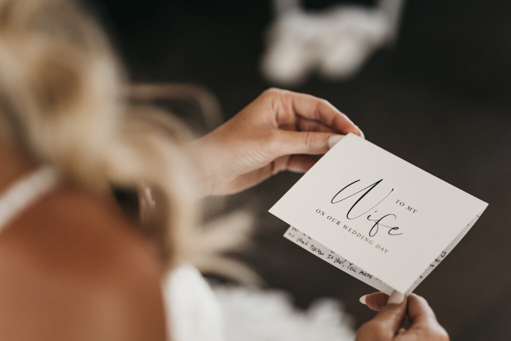 A person holds a wedding card that reads "To my wife on our wedding day," with part of a handwritten message visible inside the card.