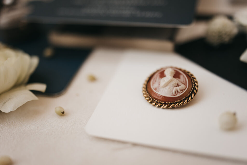 An oval cameo brooch with a gold border, featuring a carved profile of a woman, placed on a white card among scattered flower petals.