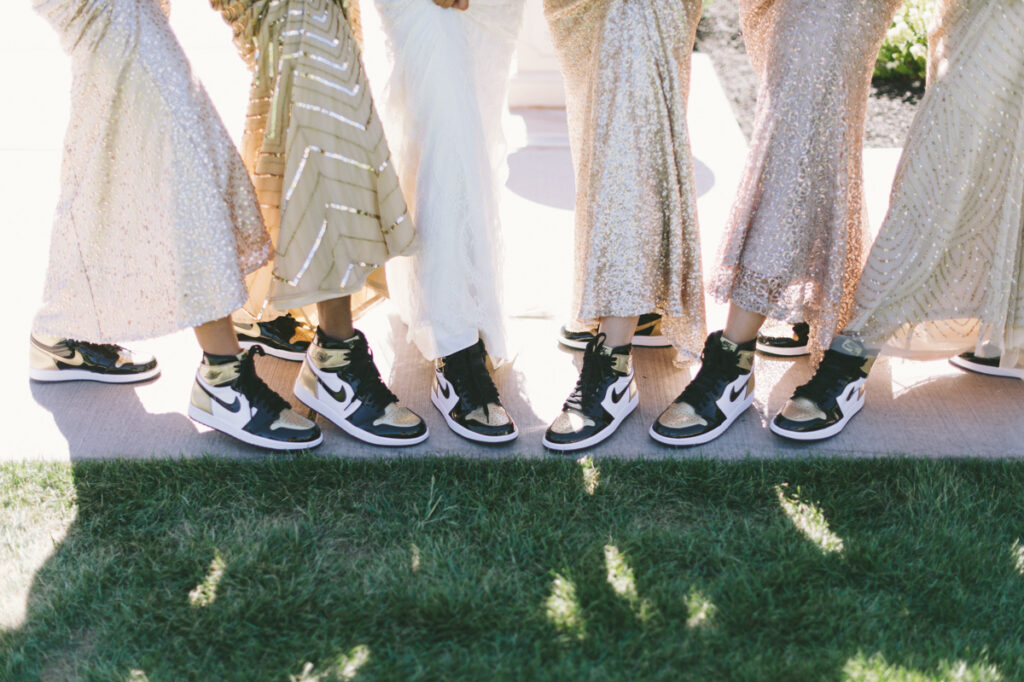 A group of people wearing gold and white dresses stand side by side on grass, all wearing black and white Nike sneakers.